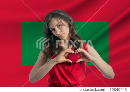 Love Maldives. A girl holds a heart on her chest in her hands against the background of the flag of Maldives. The concept of patriotism Love Maldives. A girl holds a heart on her chest in her hands against the background of the flag of Maldives. The concept of patriotism 80840443