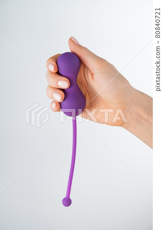 A faceless woman holding an electronic Kegel trainer for training pelvic floor muscles on a white background. Sex toy synchronized with a smartphone 80840721