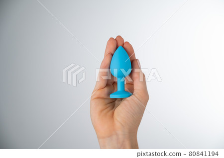 Woman holding a blue butt plug on a white background. Adult toy for alternative sex Woman holding a blue butt plug on a white background. Adult toy for alternative sex 80841194
