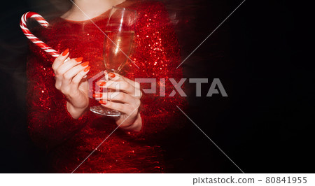 Christmas spirit. Party joy. Festive celebration. Advertising background. Unrecognizable woman holding glass of champagne candy cane long exposure blur light on black copy space. Christmas spirit. Party joy. Festive celebration. Advertising background. Unrecognizable woman holding glass of champagne candy cane long exposure blur light on black copy space. 80841955