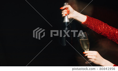 Christmas spirit. Party joy. Festive celebration. Advertising background. Female hands red spangle dress holding glass proposing bottle of champagne long exposure blur light on black copy space. Christmas spirit. Party joy. Festive celebration. Advertising background. Female hands red spangle dress holding glass proposing bottle of champagne long exposure blur light on black copy space. 80841956