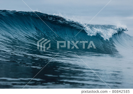 Perfect barrel wave on sandy beach. Breaking ocean wave with cloudy weather 80842585