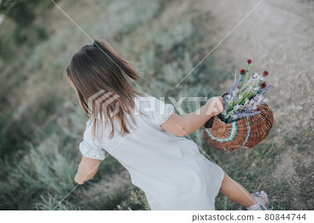 A little girl in a white dress with a wicker basket with wildflowers. A little girl in a white dress with a wicker basket with wildflowers. 80844744