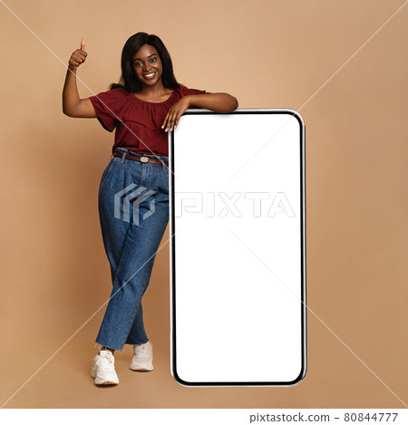 Emotional black woman posing by big smartphone with empty screen Emotional black woman posing by big smartphone with empty screen 80844777