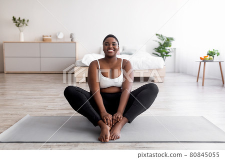 Cheerful plus size black woman doing yoga on sports mat at home, free space Cheerful plus size black woman doing yoga on sports mat at home, free space 80845055