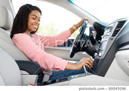 Smiling black woman driving her new car in urban city 80845096
