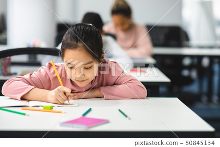 Portrait of small asian girl sitting at desk and writing Portrait of small asian girl sitting at desk and writing 80845134