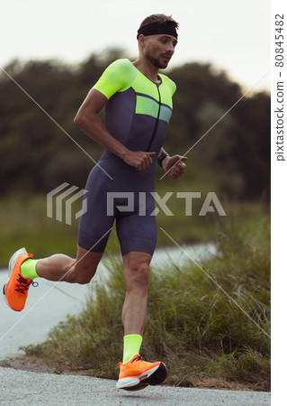 Full length image of young professional male triathlete, runner in motion on open road. Concept of sport, lifestyle, activity. Full length image of young professional male triathlete, runner in motion on open road. Concept of sport, lifestyle, activity. 80845482