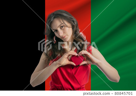 Love Afghanistan. A girl holds a heart on her chest in her hands against the background of the flag of Afghanistan. The concept of patriotism 80845701