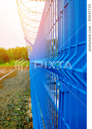Metal fencing of the production facility with barbed wire around the perimeter. Metal fencing of the production facility with barbed wire around the perimeter. 80845734
