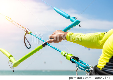 Young adult caucasian fit male person adjust kite surf board bar in sun uv protection suit on bright sunny day against blue sky at sea or ocean shore. Watersport adrenaline fun adventure acitivity Young adult caucasian fit male person adjust kite surf board bar in sun uv protection suit on bright sunny day against blue sky at sea or ocean shore. Watersport adrenaline fun adventure acitivity 80847165