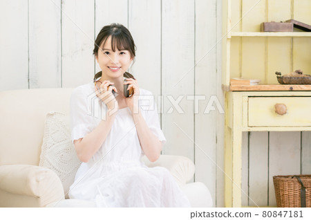 坐在沙發上，通過耳機聽音樂的年輕女人 80847181