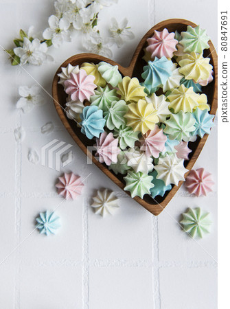 Small colorful meringues in the  wooden heartshaped bowl 80847691