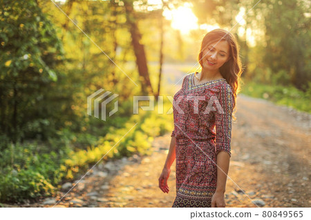 Young woman on forest path, looking down over her shoulder sun behind her, backlight creates nice bokeh in background. Young woman on forest path, looking down over her shoulder sun behind her, backlight creates nice bokeh in background. 80849565