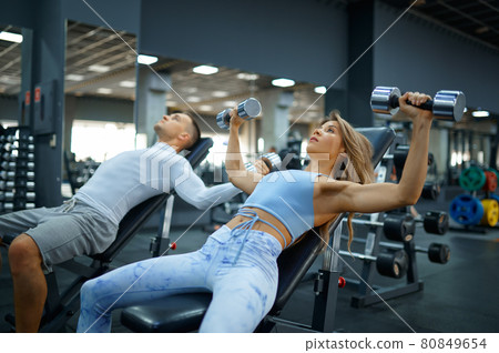 Fit couple doing exercise with dumbbells in gym 80849654