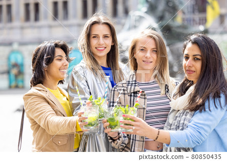 Lifestyle outdoor group of multiethnic beautiful young women clinking cocktail glasses celebrating 80850435