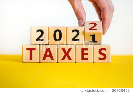 Business concept of taxes planning 2022. Businessman turns wooden cube and changes words 'Taxes 2021' to 'Taxes 2022'. Beautiful white background, copy space. Business, 2022 taxes concept. Business concept of taxes planning 2022. Businessman turns wooden cube and changes words 'Taxes 2021' to 'Taxes 2022'. Beautiful white background, copy space. Business, 2022 taxes concept. 80850491