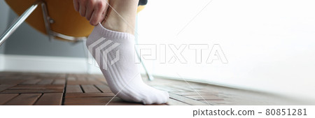 Woman puts on white short sock on her leg 80851281