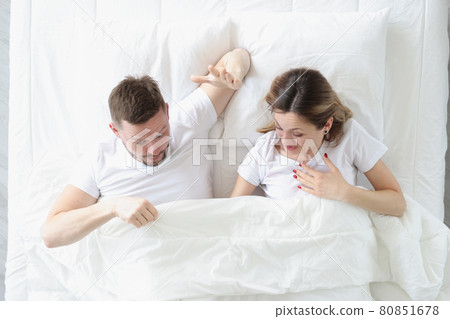 Joyful man and woman looking under blanket while lying in bed 80851678