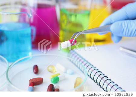 Scientist holds medical pill in forceps in laboratory closeup 80851839