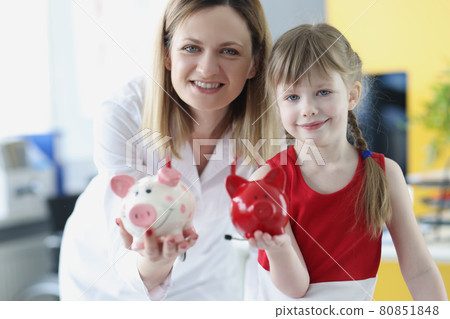Pediatrician doctor and little girl are holding pig piggy bank 80851848