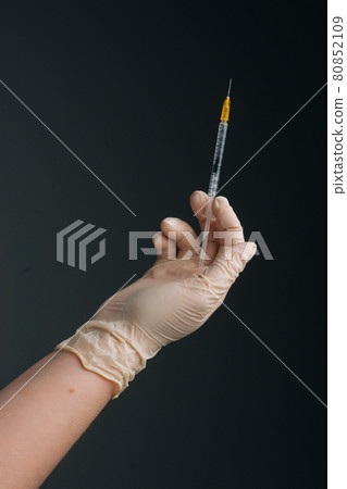 Vertical studio shot of healthcare worker with protective gloves is holding syringe, closeup on isolated black background. Vertical studio shot of healthcare worker with protective gloves is holding syringe, closeup on isolated black background. 80852109