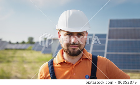Portrait of male engineer in hard helmet turning head and looking to camera. Positive worker. Ecological industry. Solar farm concept. Concept for renewable energy, technology, future. 80852879