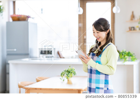 Young housewife using a smartphone in the dining / kitchen Young housewife using a smartphone in the dining / kitchen 80855339