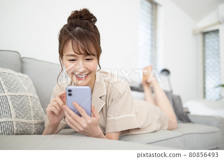一個微笑的女人在沙發上看著她的智能手機 一個微笑的女人在沙發上看著她的智能手機 80856493