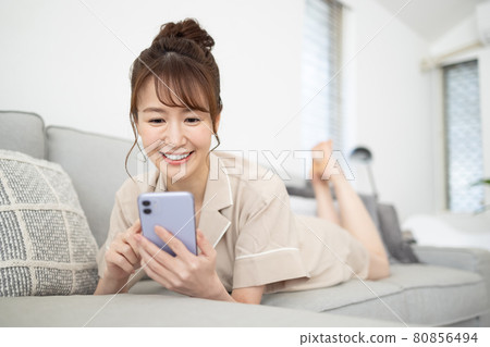 一個微笑的女人在沙發上看著她的智能手機 一個微笑的女人在沙發上看著她的智能手機 80856494
