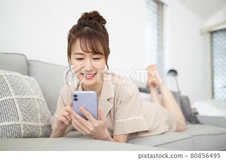 一個微笑的女人在沙發上看著她的智能手機 一個微笑的女人在沙發上看著她的智能手機 80856495