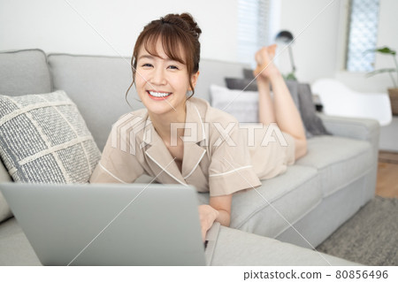 一個微笑的女人看著沙發上的電腦 一個微笑的女人看著沙發上的電腦 80856496