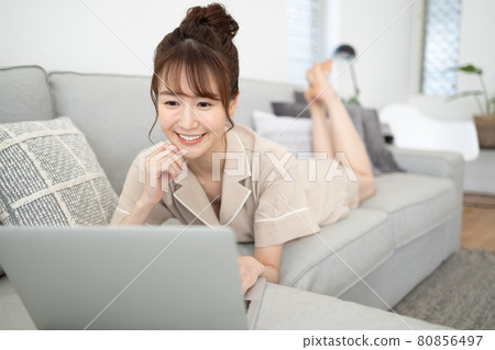 一個微笑的女人看著沙發上的電腦 一個微笑的女人看著沙發上的電腦 80856497