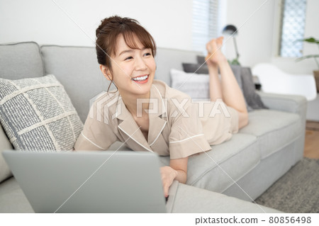 一個微笑的女人看著沙發上的電腦 一個微笑的女人看著沙發上的電腦 80856498