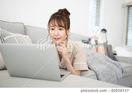 A smiling woman looking at a computer on the sofa A smiling woman looking at a computer on the sofa 80856537
