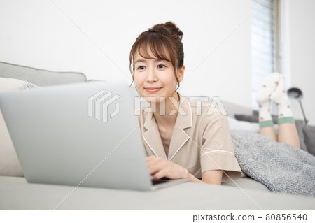 一個微笑的女人看著沙發上的電腦 一個微笑的女人看著沙發上的電腦 80856540