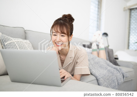 一個微笑的女人看著沙發上的電腦 一個微笑的女人看著沙發上的電腦 80856542
