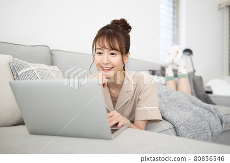 一個微笑的女人看著沙發上的電腦 一個微笑的女人看著沙發上的電腦 80856546