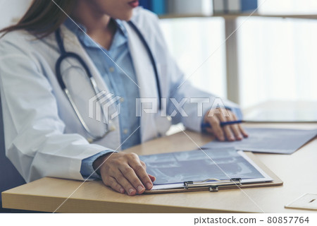Two asian women doctors discuss meeting doctor's office medical clinic looking x-ray film consulting patient disease. Asian medical lab young women talking together discussing healthcare teamwork Two asian women doctors discuss meeting doctor's office medical clinic looking x-ray film consulting patient disease. Asian medical lab young women talking together discussing healthcare teamwork 80857764