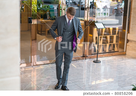 Handsome businessman in grey formal suit standing near modern building Handsome businessman in grey formal suit standing near modern building 80858206