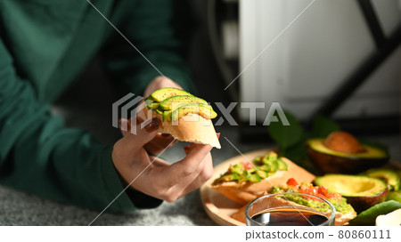 Young female sitting in kitchen and eating healthy avocado toasts. 80860111