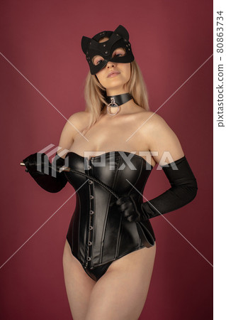 Beautiful young woman in a leather corset and cat mask posing with a whip in her hands Beautiful young woman in a leather corset and cat mask posing with a whip in her hands 80863734