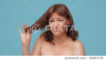 Unhappy beautiful woman holds of hair ends looking at camera. Pretty nude mature woman on color back. Hair care concept Unhappy beautiful woman holds of hair ends looking at camera. Pretty nude mature woman on color back. Hair care concept 80865746