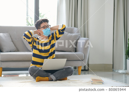Asian man sitting on floor and working on laptop with books Asian man sitting on floor and working on laptop with books 80865944