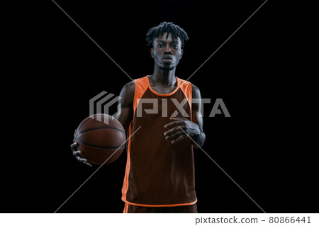 Studio shot of one professional african basketball player posing with ball isolated over dark studio background. 80866441