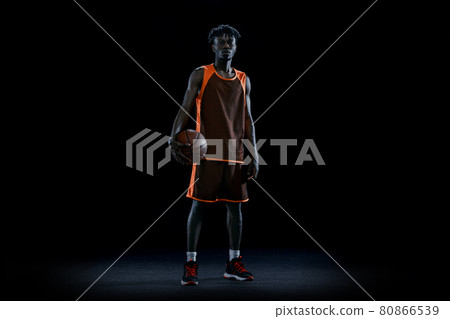 Young african man, professional basketball player posing with ball isolated over dark studio background. Young african man, professional basketball player posing with ball isolated over dark studio background. 80866539