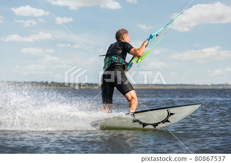 Young adult caucasian fit male person enjoy riding kite surf board in sun uv protection suit on bright sunny day against blue sky at sea or ocean shore. Watersport adrenaline fun adventure acitivity 80867537