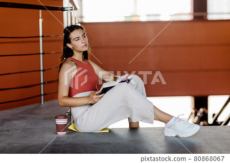 A pretty student girl with a textbook and a cup of coffee is sitting on the stairs A pretty student girl with a textbook and a cup of coffee is sitting on the stairs 80868067