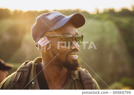 In summer in nature. Close-up young african man walking, strolling alone in forest, meadow, field. Amazing landscape views. Active lifestyle, hobby, weekend travel concept 80868799