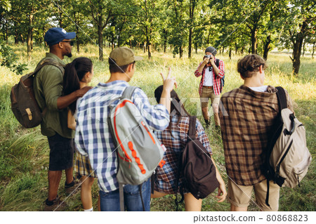 Group of friends, young men and women walking, strolling together during picnic in summer forest, meadow. Lifestyle, friendship, 80868823